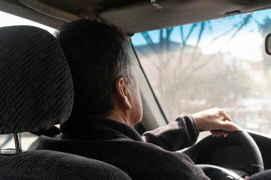Perfil de cara, casi de espaldas manejando un carro, hombre mayor, detalle de rostro y mano, cabello con canas, d&iacute;a soleado, interior de carro, tim&oacute;n de carro