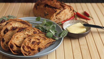 Sliced bread with tomato and olives baked inside, paired with vegan butter, chili, fresh greens. Mediterranean-inspired vegan meal is healthy eco-friendly option filled with plant-based goodness 