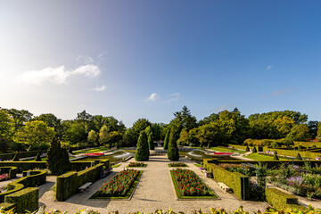 Panoramic landscape of Arcen Castle Gardens, fountain, flowers, pedestrian paths and green leafy trees against blue sky in background, sunny day in Limburg, Netherlands