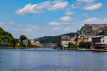 Obraz premium View of Meuse river with cityscape of Dinant resort town and citadel on top of rocky mountain against blue sky in background, lush trees on hill, sunny summer day in Namur province, Wallonia, Belgium