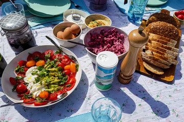 Picnic table with variety of food, Mediterranean salads, boiled eggs, jam and bread, lunch outdoors on garden terrace, enjoying a sunny summer day