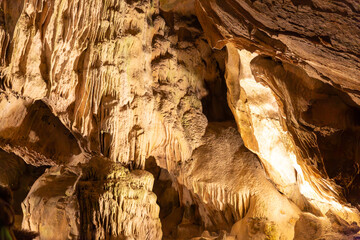 Underground rock formations in Remouchamps caves, cracked, rough and uneven walls due to erosion and water seepage, illuminated with artificial light, Aywaille, Belgium