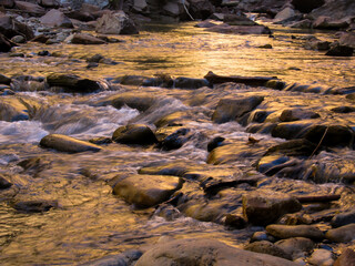 Fast flowing river over the boulders, gold coloured due to the reflection of the surrounding sandstone cliffs