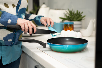 Close-up of a woman’s hands using a knife to spread butter on a turquoise frying pan for cooking eggs.