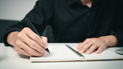 Fototapeta premium Male hand taking notes on the notepad. businessman working at work table, checklist writing planning investigate concept. focus on man hand holding pen, putting signature at official paper