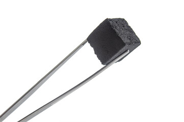Charcoal cube for hookah in forceps isolated on white background
