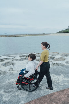 車椅子に乗った日本人女性が友人の女性と夏の沖縄を旅を楽しんでいる