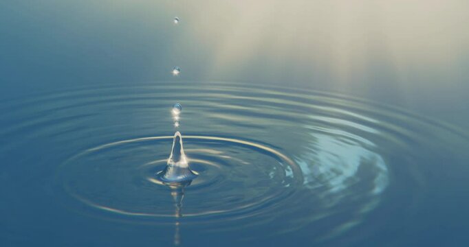 A single drop of water falls into a calm, mirror-like surface of the sea, creating gentle concentric ripples and a soft splash. The serene scene captures the peaceful interaction of water and motion, 