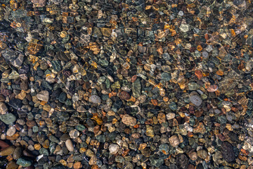 Beautiful stones on the bottom are visible through the transparent water. Play of light and reflections. A whimsical natural background.