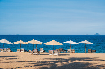 beach umbrellas with sun beds without people on a sandy beach against the background of the sea or ocean