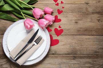 Table setting for romantic Valentine's day celebration, top view. Plates, cutlery, flowers and hearts on wooden table, space for text