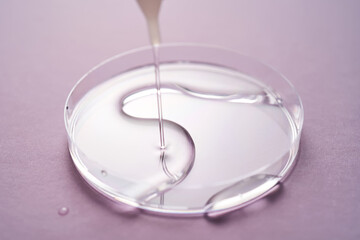 Serum or cosmetic oil flows into a transparent bowl on a purple background.