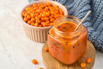 Sea buckthorn jam in a jar, spoon, whole sea buckthorn berries, scarf on a light background....