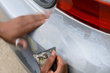 Repairing a scratched car bumper with a putty knife in a residential garage during daylight hours