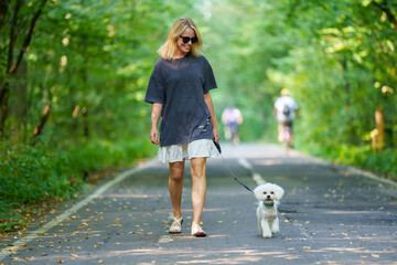 Girl walking the dog in the park forest. Rest concept. Woman walking with a dog on a leash during a good day
