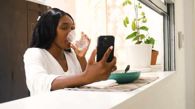 Young woman eating lentils at home looks dismayed as she scrolls on her phone