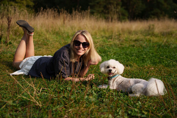 The beautiful woman lies on the grass and hug with her dog. The girl have a fun tome with the dog....