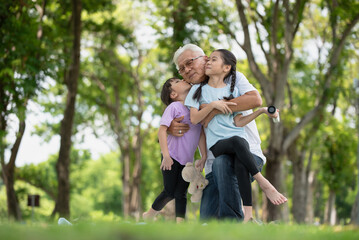 Happy Asian family children having fun and kissing her grandfather on the cheek in the park