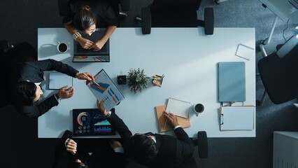 Top down aerial view of smart manager pointing at financial graph on whiteboard while diverse business team explain and plan marketing idea at meeting table with stock market statistic. Directorate.