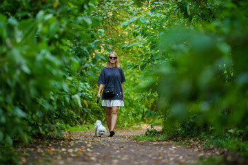 Girl walking the dog in the park forest. Rest concept. Woman walking with a dog on a leash in blue dress and with shoes.