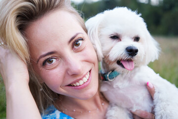 Portrait of smiling young woman kiss dog in Natural Park. Dog lover woman wearing blue dress with dog during good day. Concept of friendship and beautiful girl with a small dog