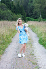 Portrait of smiling young woman kiss dog in Natural Park. Dog lover woman wearing blue dress with dog during good day. Concept of friendship and beautiful girl with a small dog