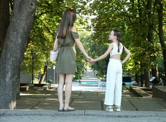 Fototapeta premium Mother and daughter holding hands in park, back view