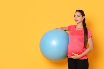 Beautiful pregnant woman with fitball on yellow background, space for text