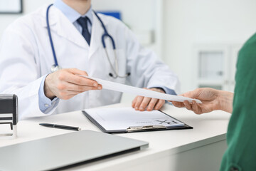 Doctor giving prescription to patient at white table in clinic, closeup