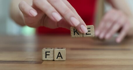 Woman hands removes letters from word Fact making Fake using wooden cubes. Dangers of misinformation and importance of verifying sources - Powered by Adobe