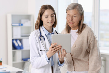 Smiling healthcare worker and senior patient checking analysis results on tablet in hospital