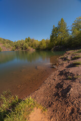 Peaceful forest Kamyki lake after old quarry reflecting the vibrant green foliage under a clear blue sky, creating a serene and tranquil atmosphere © Pawel-Wierzchowski