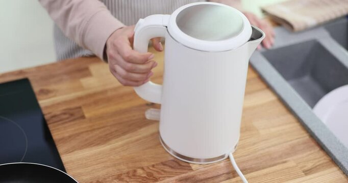 Young woman sets electric kettle on stand in kitchen at home. Housewife ready to plug in and heat water anticipating warmth of freshly brewed tea