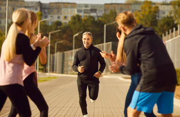 Obraz premium Diverse group of people jogging together in a city park, engaged in outdoor training. Spirit of teamwork and sport, showing individuals working out and running together in a urban outdoor setting.
