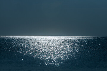 Fototapeta premium The suns light sparkles across the surface of calm ocean waters, creating a serene and shimmering horizon. The peaceful, minimalist seascape exudes tranquility with its soft reflection of light.