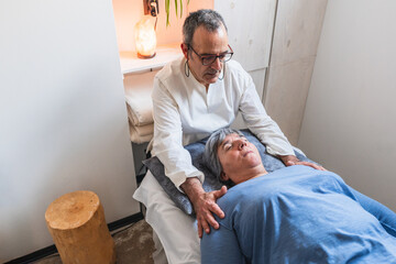 Elderly practitioner performing craniosacral therapy on patient with gentle chest support in calm clinic.