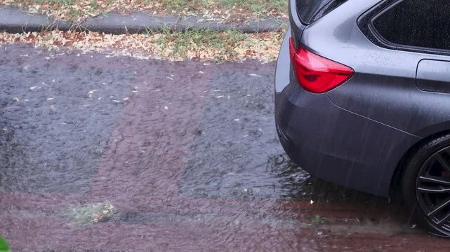 Heavy rain causes flooding on the street. A small stream flows past a parked car