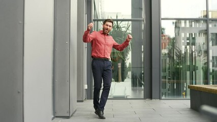 Joyful businessman dancing outside office on city street. Handsome bearded man expressing celebration and happiness. Excited male worker celebrating victory. Concept of success, and positive energy