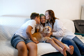 Mother and her two sons are sitting on the sofa having fun, making faces, fooling around, laughing,...