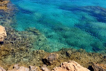 Empty rocky shoreline with stones, clear calm paradise sea. Turquoise ocean, vacation destination without people. Paradise shore with clear water, travel photography.