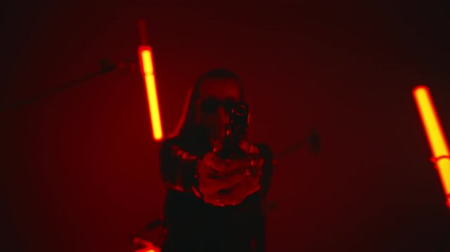 Beautiful badass lady agent in leather coat and sunglasses aiming a gun in a dark room with red tube lights