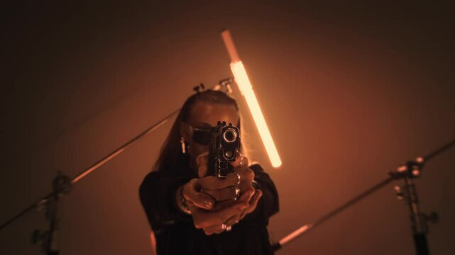 Dangerous female hitman aiming with a handgun in a dark room