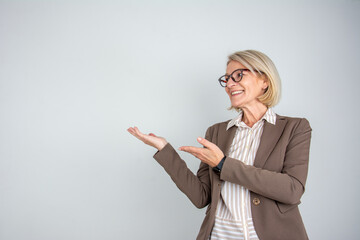 Mature beautiful blonde woman wearing business clothes over grey isolated background pointing aside with hands open palms showing copy space, presenting advertisement smiling excited happy See Less