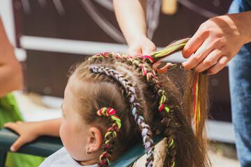 Girl hairdresser braids colorful ropes into little girl's hair