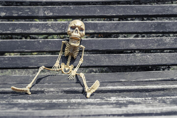scary skeleton on a bench in an autumn garden with space for an invitation to a Halloween costume...