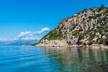 Small ship sails along rocky shore. Transparent water in  sea. Croatia.