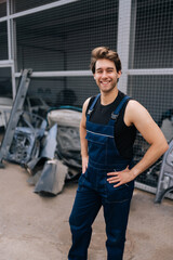 Fototapeta premium Vertical shot of cheerful male repairman in uniform standing posing in auto service shop, looking at camera with smiling expression. Concept of professional automobile maintenance in repair center.