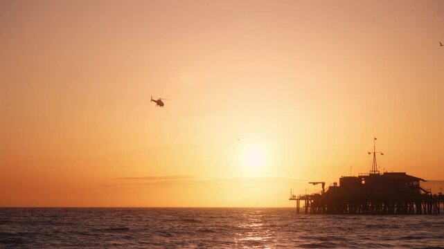LAPD helicopter flying over Santa Monica pier during a scenic sunset in Los Angeles, California, USA