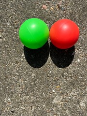 A red and a green ball lie on a grey stone floor and cast shadows