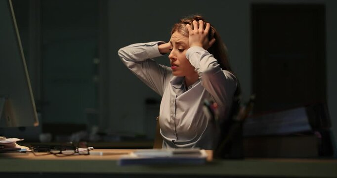 Frightened woman worker clutches head sitting in office late at night. Lady overwhelmed by deadline pressure and panic of losing essential financial data